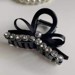 Detail of elegant black resin hair claw clip with rhinestones and ribbon bow