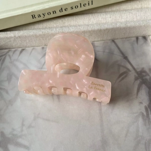 Détail de la pince à cheveux en acétate rose marbré avec inscription dorée élégante