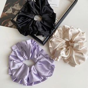 Lot de trois chouchous en satin noir, violet et doré sur un plateau de présentation