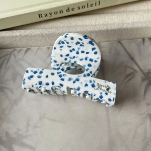 Détail d'une pince à cheveux en acétate marbré bleu avec lettrage doré élégant