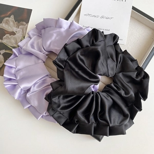 Détail de chouchous en satin lavande et noir avec bords ondulés dans un plateau blanc