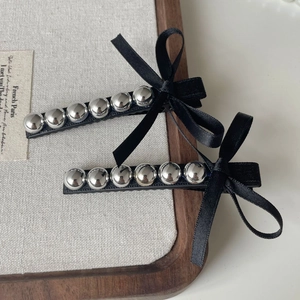 Détail de deux barrettes à nœuds en satin noir avec décorations de perles métalliques