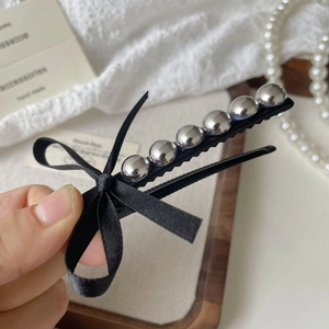 Détail d'une barrette à nœud en soie noire avec perles argentées sur un plateau