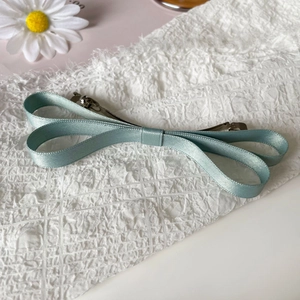 Close-up of light blue satin bow hair clip with silver metal alligator base on white fabric