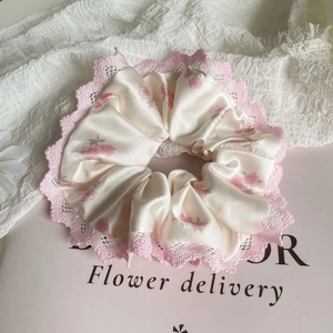 Détail d'un chouchou rose fleuri en satin avec bordure en dentelle et texture soie