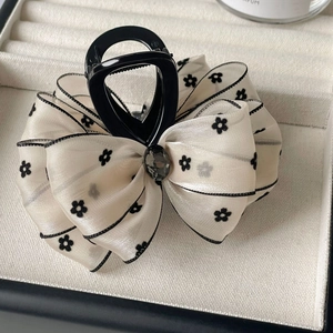 Detailed macro view of cream satin bow hair claw with black floral patterns and center gemstone