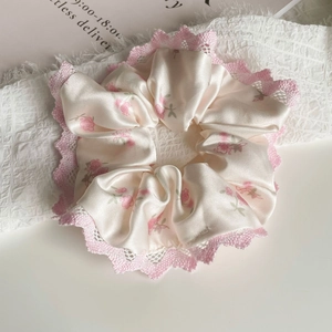 Détail d'un chouchou en satin crème avec imprimé de roses roses et bordure en dentelle