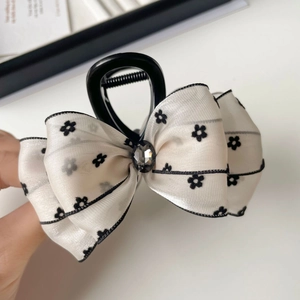 Detail of white satin bow hair claw with black floral embroidery and center rhinestone