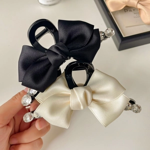Detail view of satin bow hair claws in black and cream with sparkling rhinestones