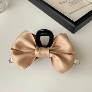 Detail of champagne satin ribbon hair claw clip with rhinestones on white surface