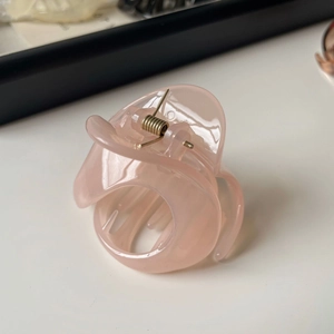 Gros plan d'une pince à cheveux rose translucide avec ressort en métal doré durable