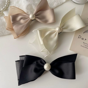 Close-up of elegant satin bow hair clips with pearls in black, white, and champagne colors