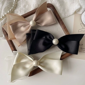 Three elegant satin and organza bow hair clips with pearls in black, beige, and champagne
