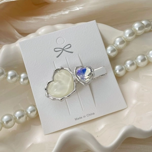 Detailed close-up of a silver hair clip with cream heart and iridescent crystal on a tray