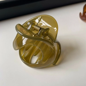 Détail d'une pince à cheveux spirale vert olive translucide avec ressort en métal doré