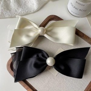 Detail of elegant satin bow hair clips with pearls on a luxury textured tray