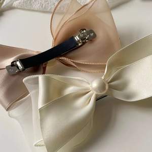 Detailed macro view of elegant satin bow hair clips with pearls and duckbill metal fasteners
