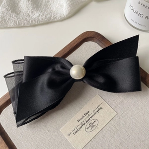Detail of elegant black satin and mesh bow hair clip with a centered pearl decoration