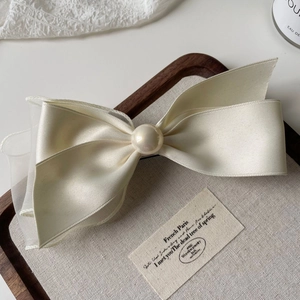 Detail of beige satin and mesh bow hair clip with a central pearl in a wooden tray