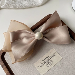 Close-up of champagne satin and mesh ribbon bow hair clip with a large pearl detail