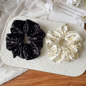 Close-up of black and cream satin polka dot scrunchies on a textured white tray