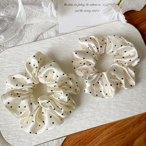 Detailed macro of two beige satin polka dot scrunchies on a textured white ceramic tray