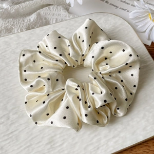 Detailed view of cream satin scrunchie with black polka dots on ceramic dish