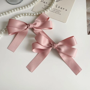 Detail view of pink satin bow hair clips with silky texture on a white background