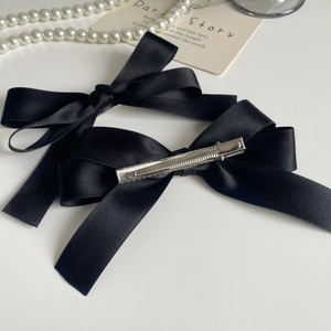 Detail of two black satin bow hair clips showing glossy silk texture and metal clip