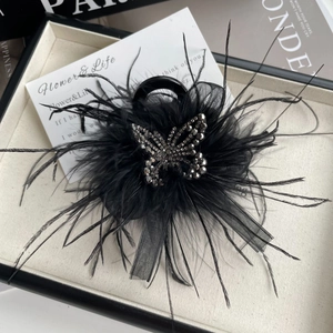 Vue détaillée d'une pince à cheveux noire avec plumes et strass sur un coffret cadeau