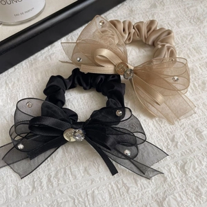 Détail de chouchous élégants avec nœud en organza noir et champagne avec charms en cristal