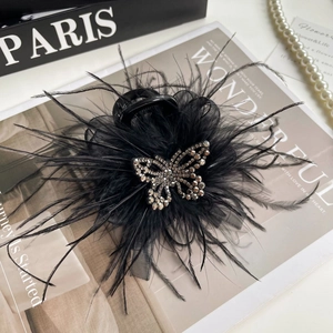 Détail de la pince à cheveux avec plumes noires, papillon en strass et ruban en maille