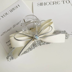 Detail of cream bow hair claw with silver edges, pearls, and sparkling crystals