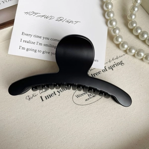Détail d'une grande pince à cheveux noir mat présentée sur un fond en tissu crème