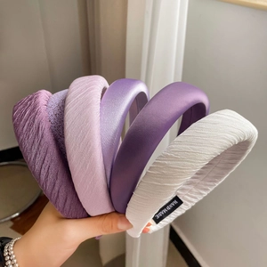 Detail showing five assorted satin headbands in shades of purple and white with handmade labels
