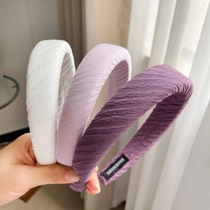 Close-up of three handmade satin headbands in white and purple with pleated texture