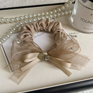 Détail d'un chouchou élégant en organza champagne avec nœud et strass sur plateau
