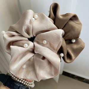 Detailed view of satin scrunchies with white pearls in champagne and dark brown colors