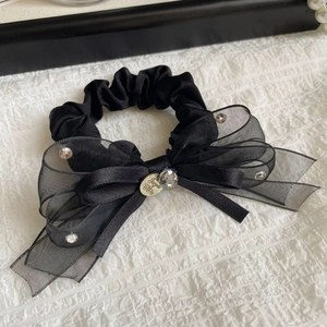 Détail d'un chouchou en organza noir avec strass brillants et breloque dorée