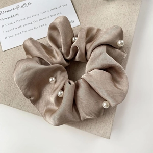 Detail of champagne satin scrunchie with white pearls on a textured linen background