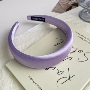 Close-up of a purple satin sponge headband with a handmade woven label on a book