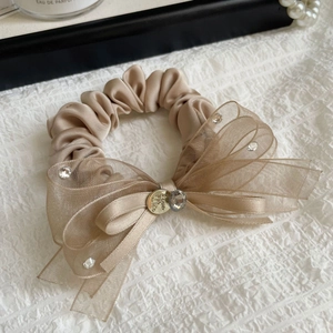 Détail d'un chouchou en satin champagne avec nœud en organza et accents de strass