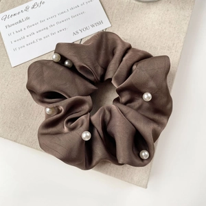 Detail of coffee brown satin scrunchie with elegant pearl accents on beige fabric