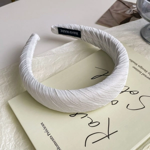 Detail of a thick white pleated satin headband on a book with a Hand Made label tag