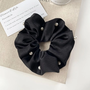 Detail of a black satin scrunchie with white pearls on a minimalist beige background
