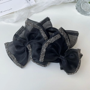 Macro detail of elegant black organza bow hair claw clip with shimmering rhinestone edges