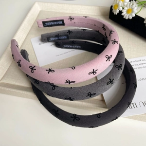 Détail de trois serre-têtes en éponge faits main rose, gris et noir avec motifs nœuds