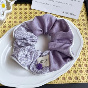 Détail d'un chouchou à fleurs lilas avec texture satinée et étiquette tissée