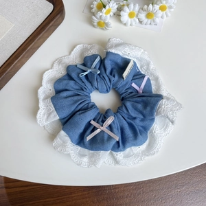 Détail d'un chouchou en denim avec bords en dentelle, nœuds en satin et étiquette fait main