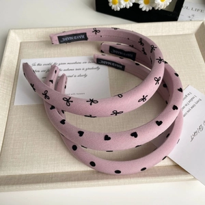 Détail de trois serre-têtes roses en tissu avec motifs de cœurs, pois et nœuds